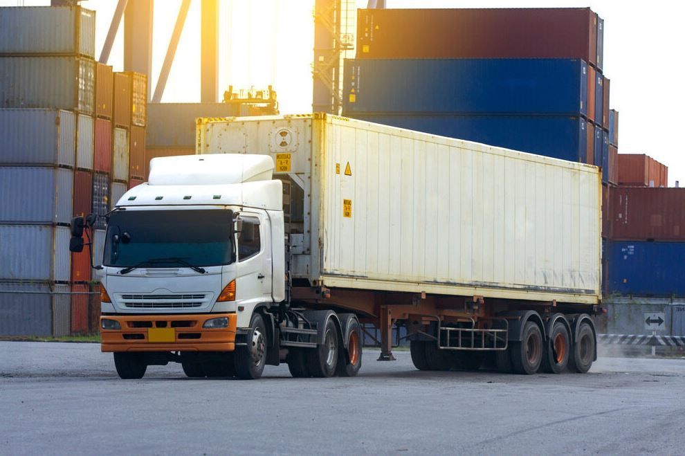 A Semi Truck is Driving Down a Road Next to a Row of Shipping Containers — Supersonic Couriers In West Mackay, QLD