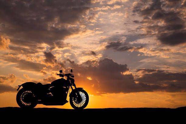 A motorcycle is parked on the side of the road at sunset.