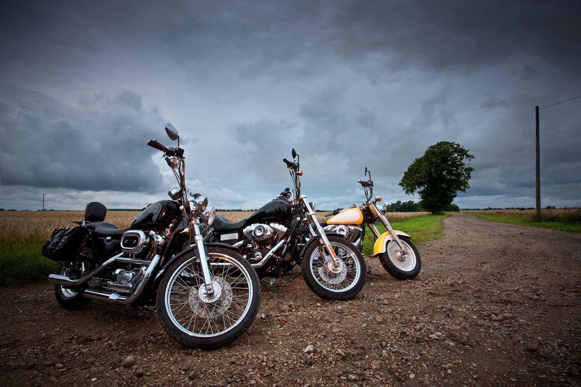 Three motorcycles are parked on the side of a dirt road.