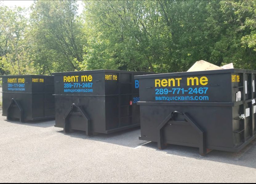 Three black dumpsters lined up on pavement, each with