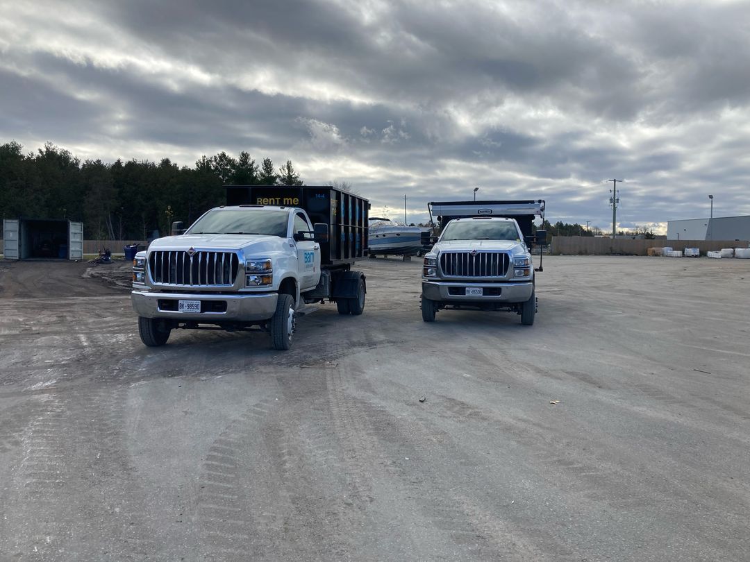 Two white dump trucks parked on a gravel lot under a cloudy sky.