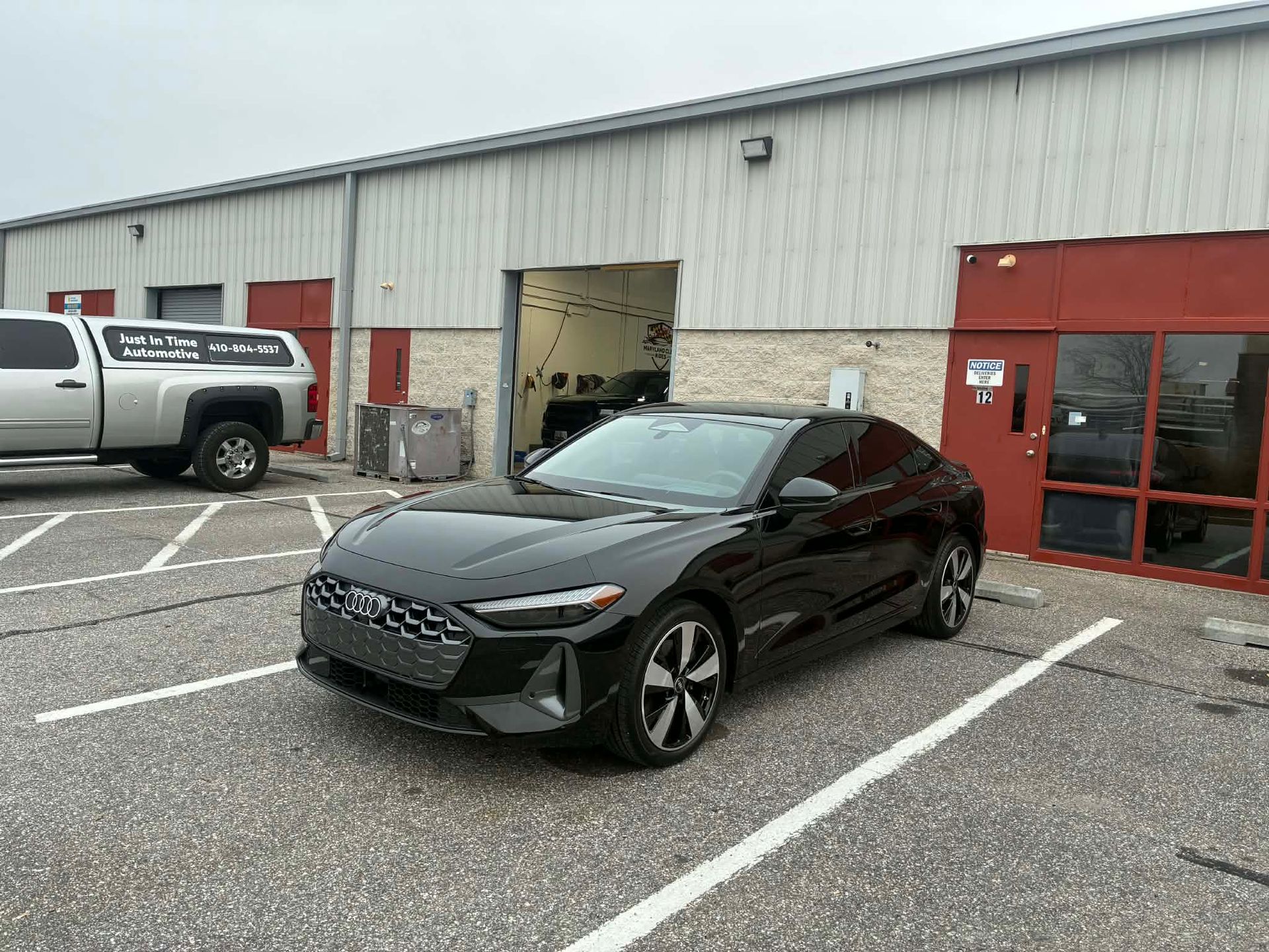 Black Audi sedan parked in front of a gray building with a loading bay.