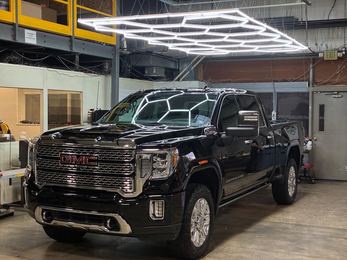 A white truck and black sports car in a modern garage with a second-story platform.