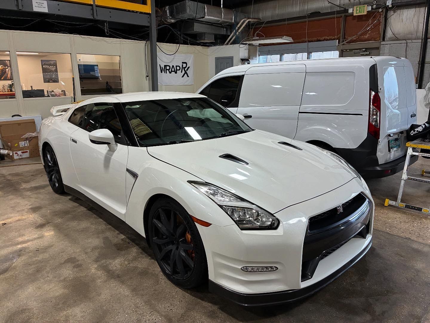 White Nissan GT-R sports car parked in a garage with a white van in the background.