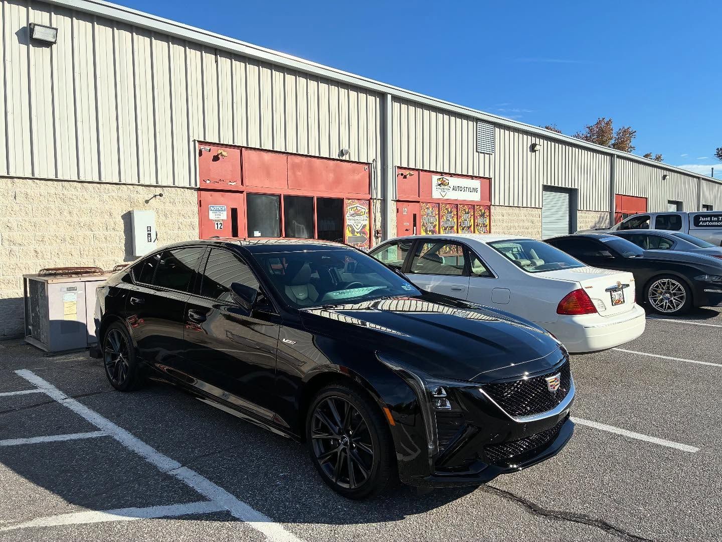Black Cadillac sedan parked in front of a building with other cars on a sunny day.
