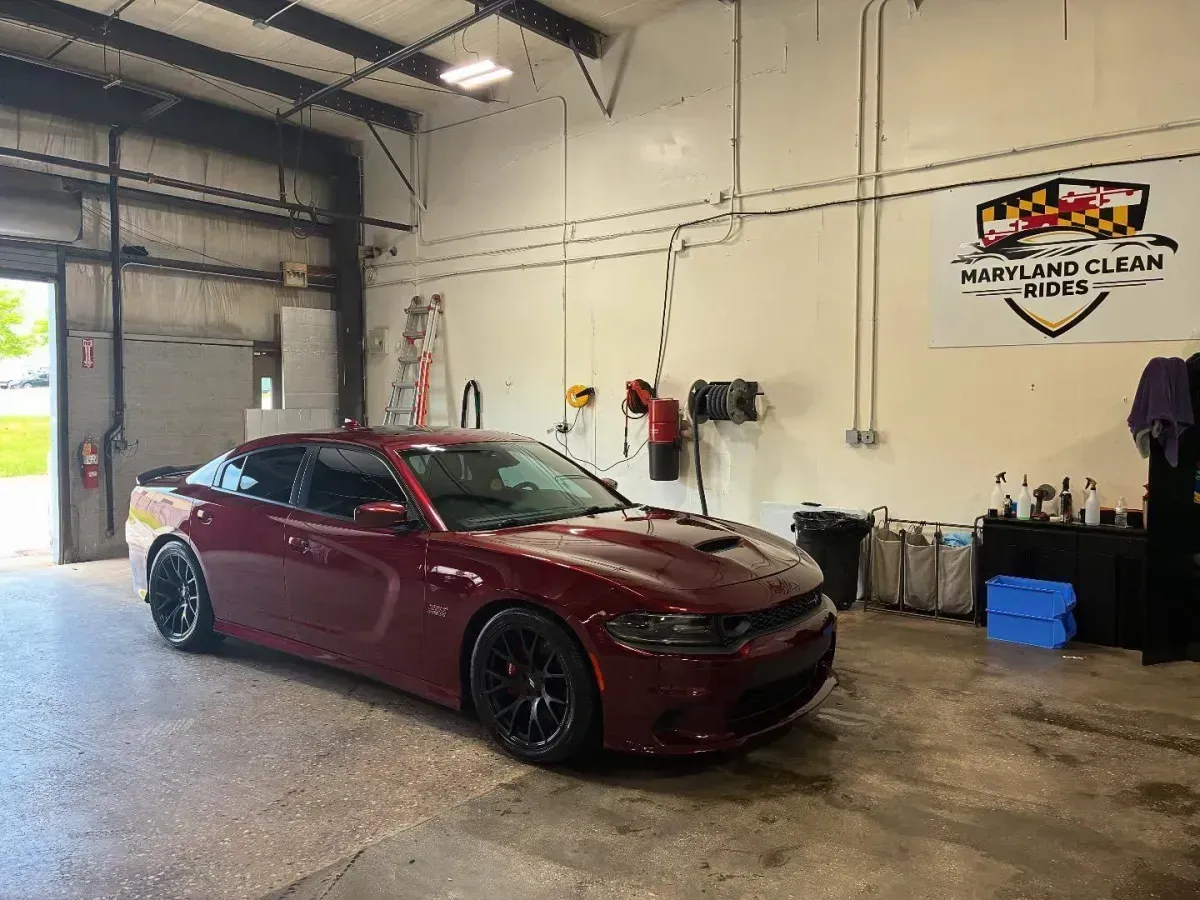 A red Dodge Charger in a car wash bay with Maryland Clean Rides sign.