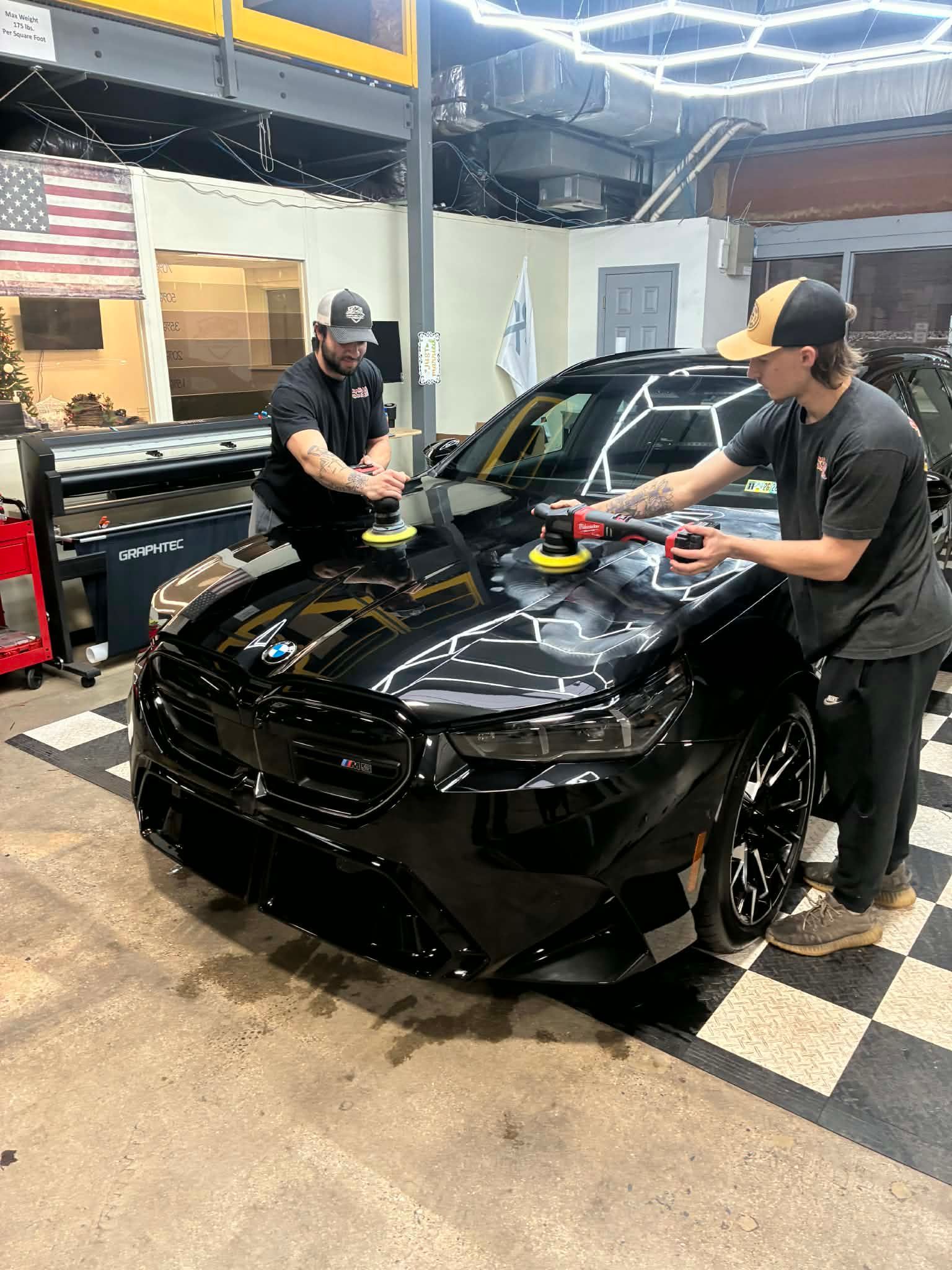 Two people polishing a black BMW in a shop.