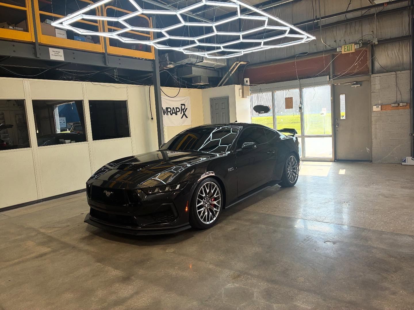 Black sports car parked inside a garage, under honeycomb-shaped lights.