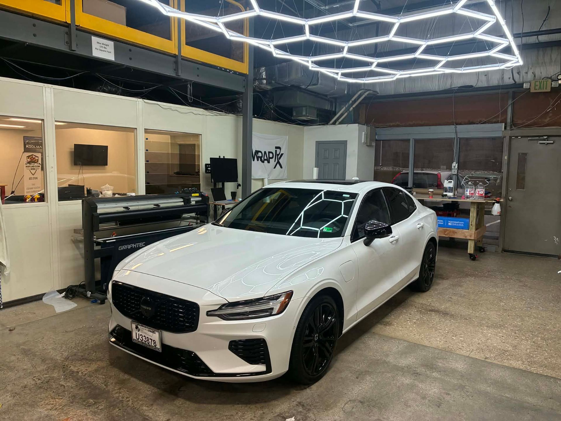 White Volvo sedan in a garage under hexagonal lights.