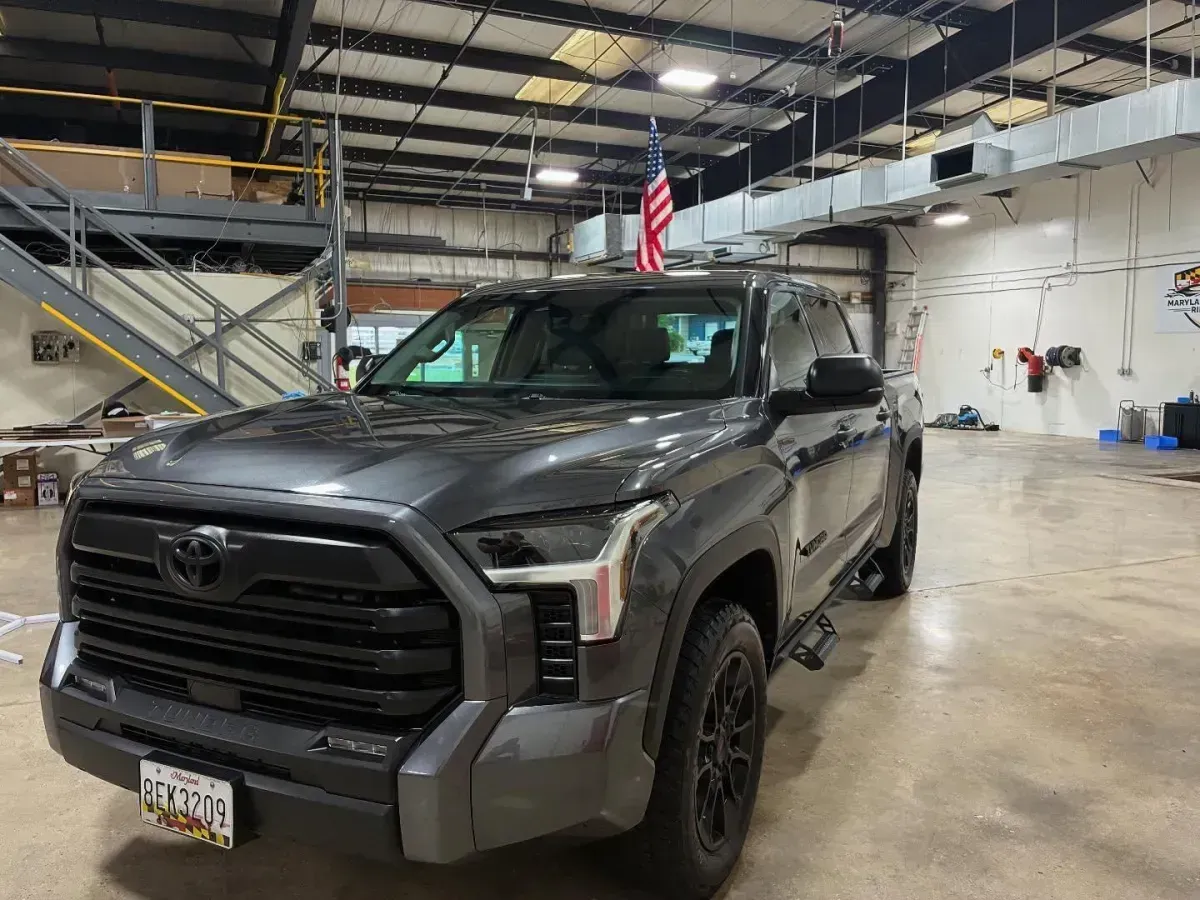 Dark gray Toyota Tundra truck with an American flag on the roof, inside a large warehouse.