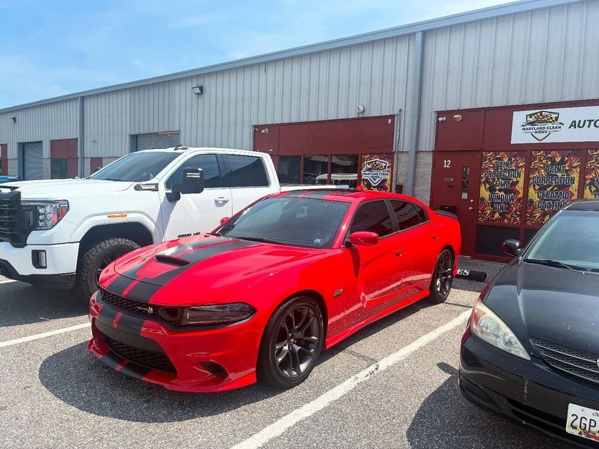 Red Dodge Charger parked outside a building, with a white pickup truck on the left.