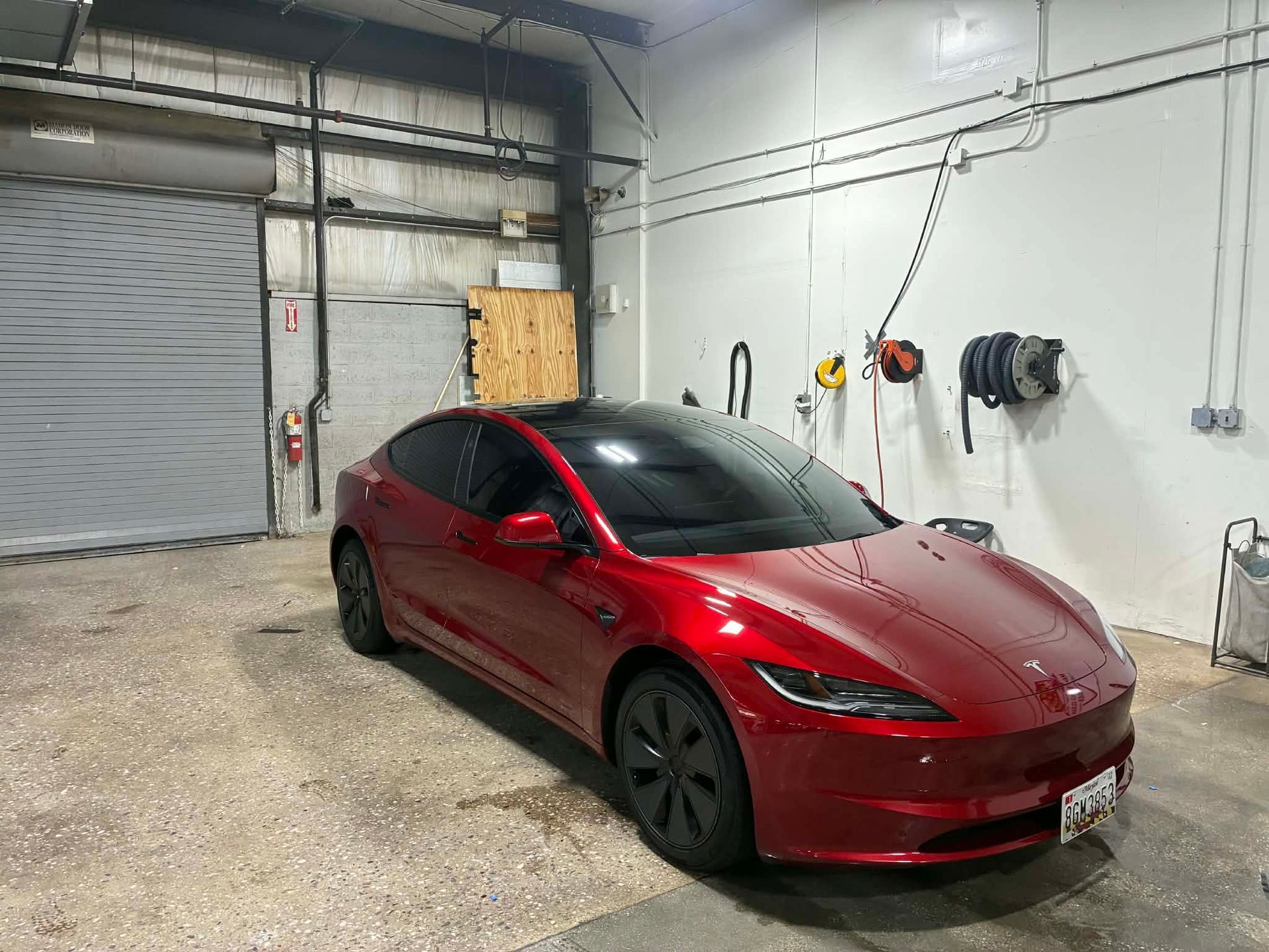 Red Tesla car inside a garage with a roll-up door and equipment.