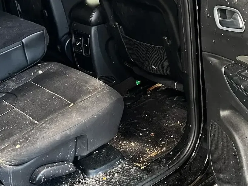 Dirty black car interior with food debris on seats and floor mats.