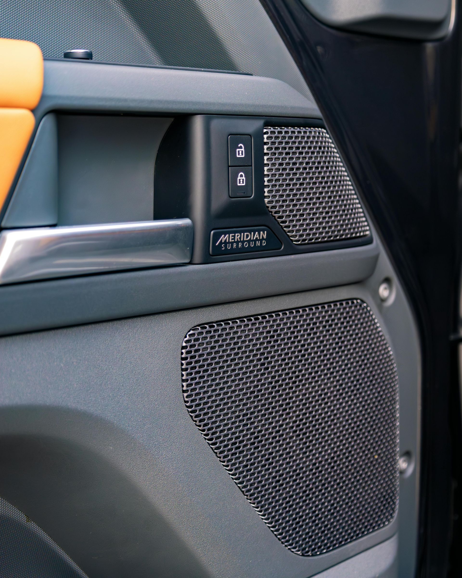 Car door interior: gray panel with metal speaker covers, handle, lock buttons, and yellow trim.