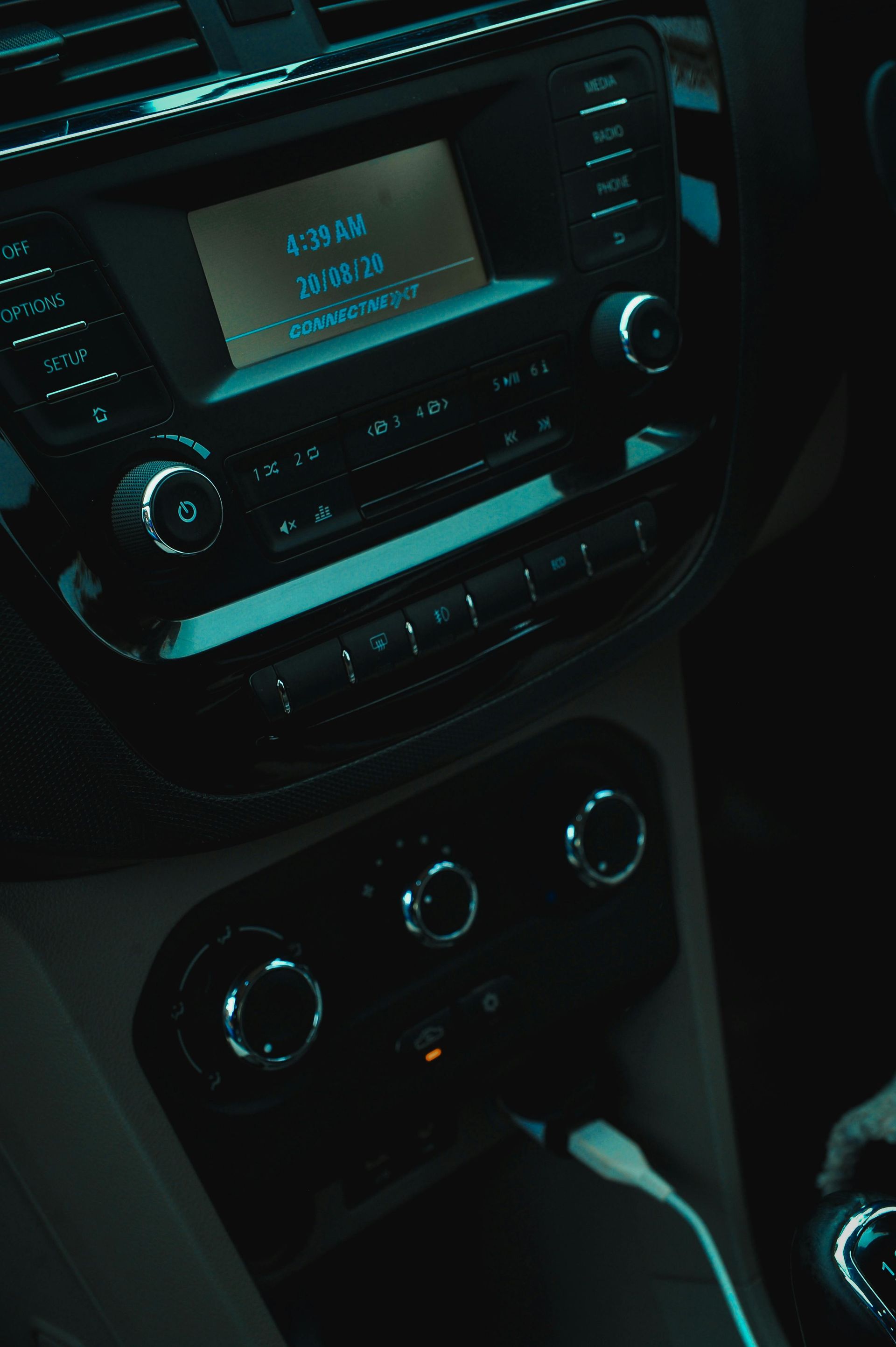 Car dashboard interior with radio display, dials, and controls illuminated in blue light.