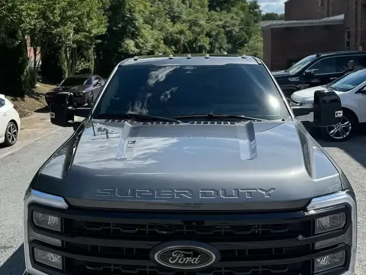 A gray Ford Super Duty truck parked on an asphalt lot, other vehicles in background.