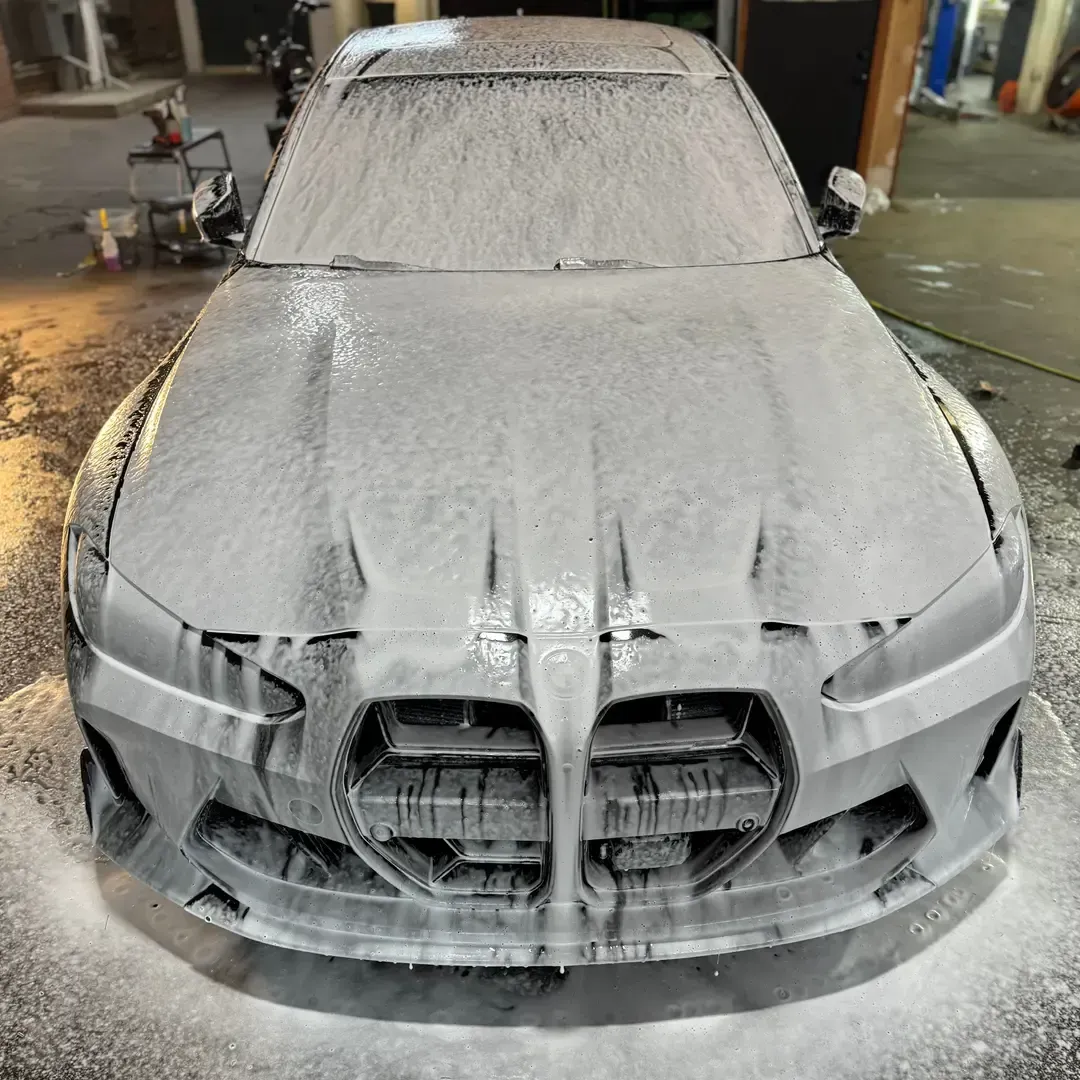 Car covered in foam being washed, with distinctive front grille visible.