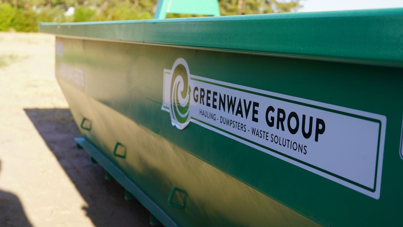 A man is standing in front of a green dumpster.