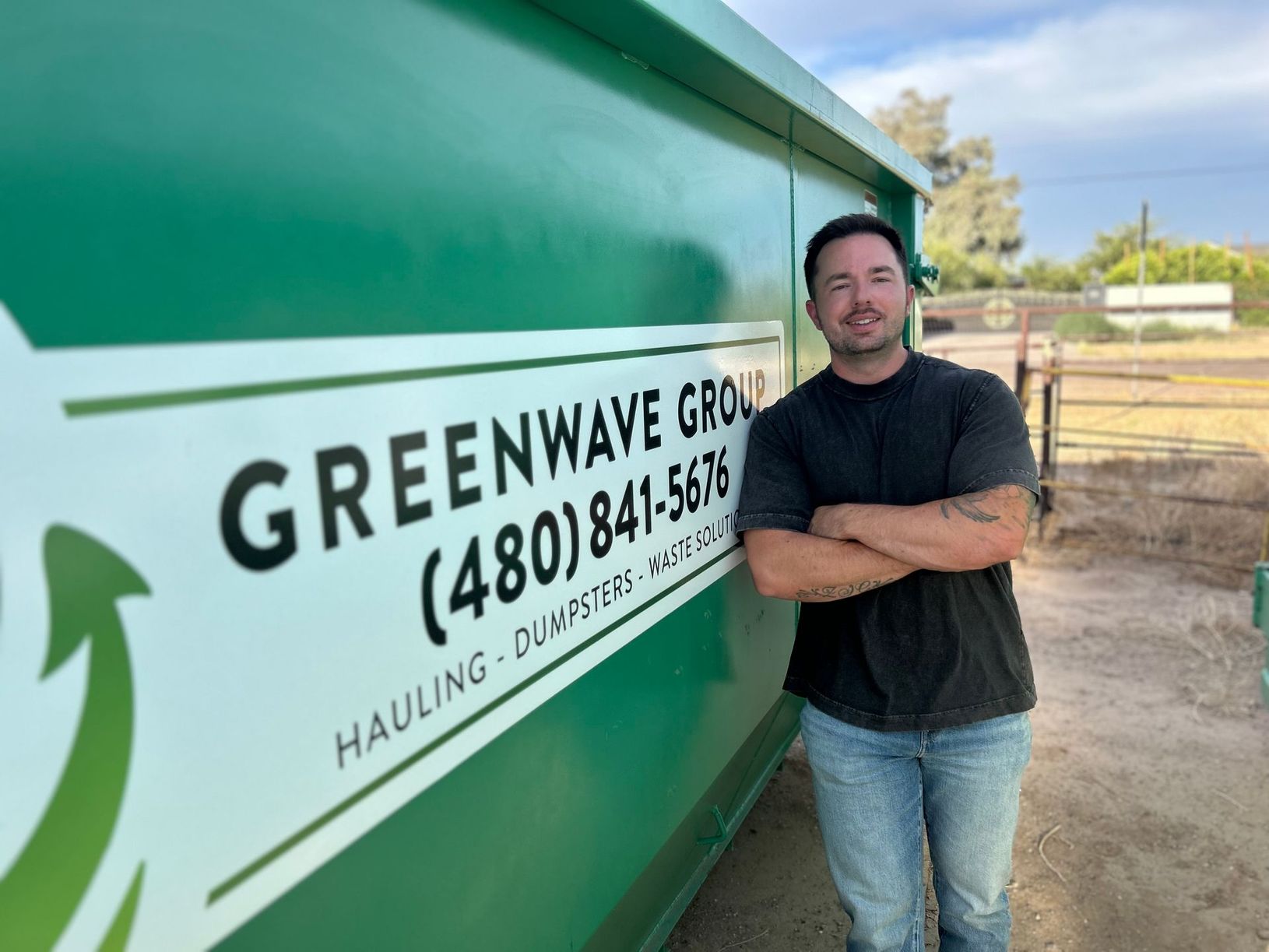 A man is standing in front of a green dumpster.