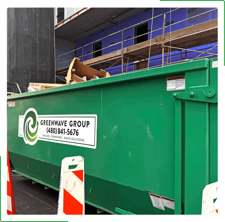 Green dumpster with white lettering, in front of a building under construction.
