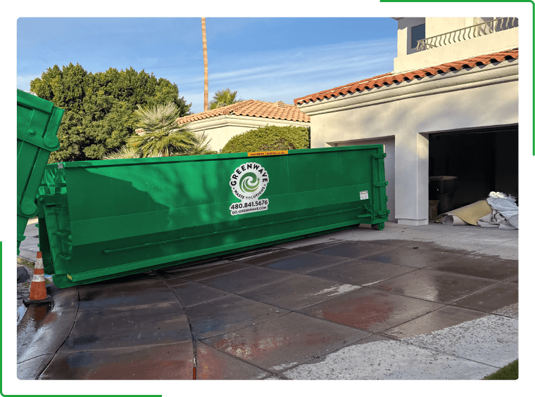 A green dumpster filled with cardboard boxes is sitting on the side of the road.
