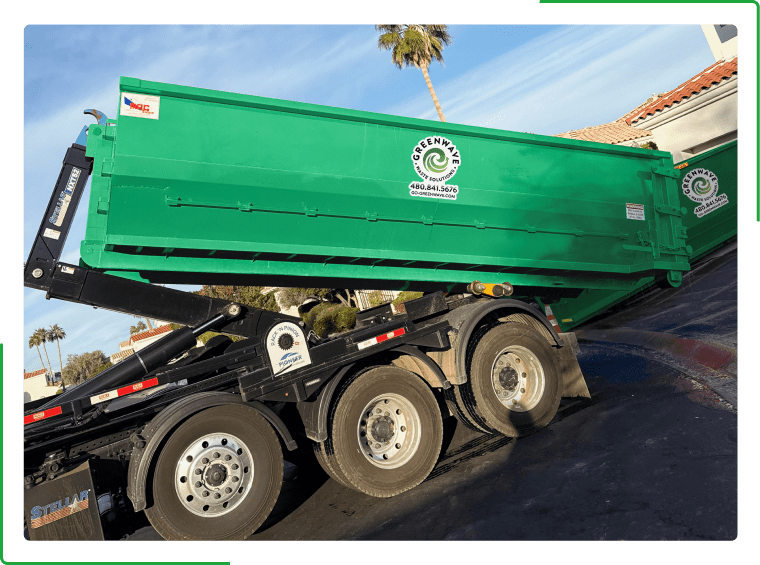 A green dumpster filled with cardboard boxes is sitting on the side of the road.