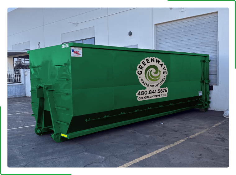 A green dumpster filled with cardboard boxes is sitting on the side of the road.