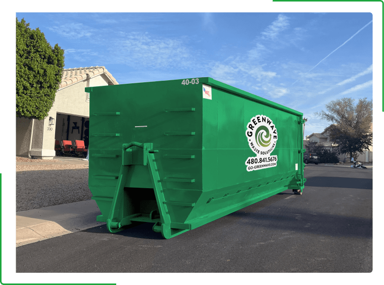 A green dumpster filled with cardboard boxes is sitting on the side of the road.