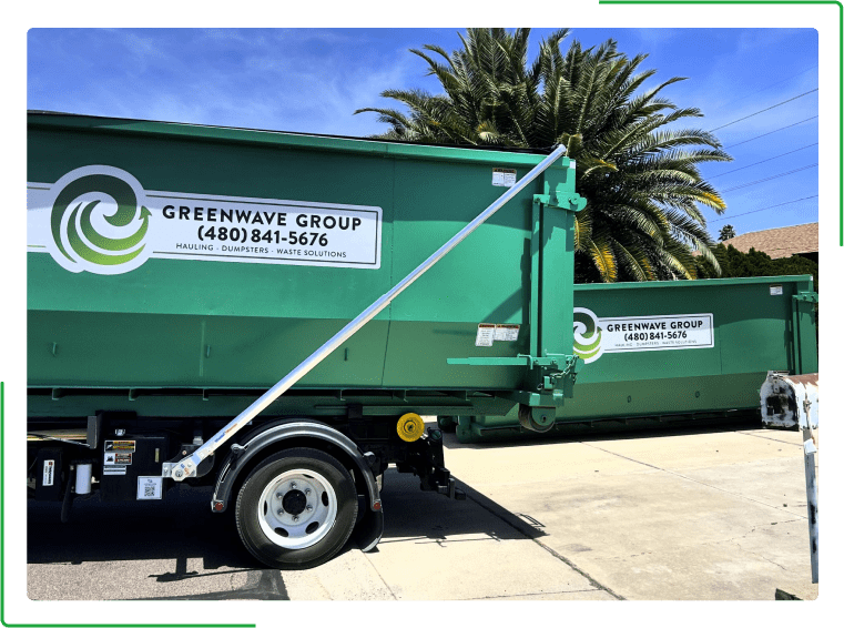 A green dumpster filled with cardboard boxes is sitting on the side of the road.