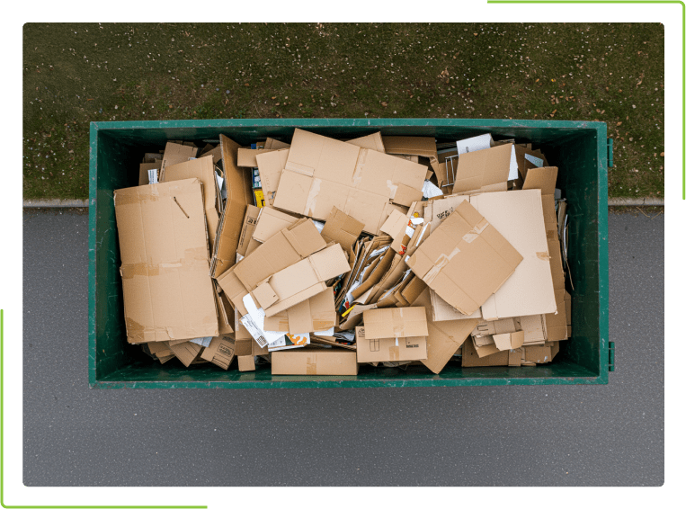 A green dumpster filled with cardboard boxes is sitting on the side of the road.