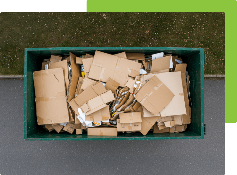 A green dumpster filled with cardboard boxes is sitting on the side of the road.