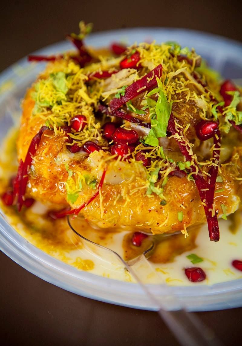 Close-up of a kachori chaat, topped with sev, pomegranate, chutney, and yogurt in a plastic bowl.