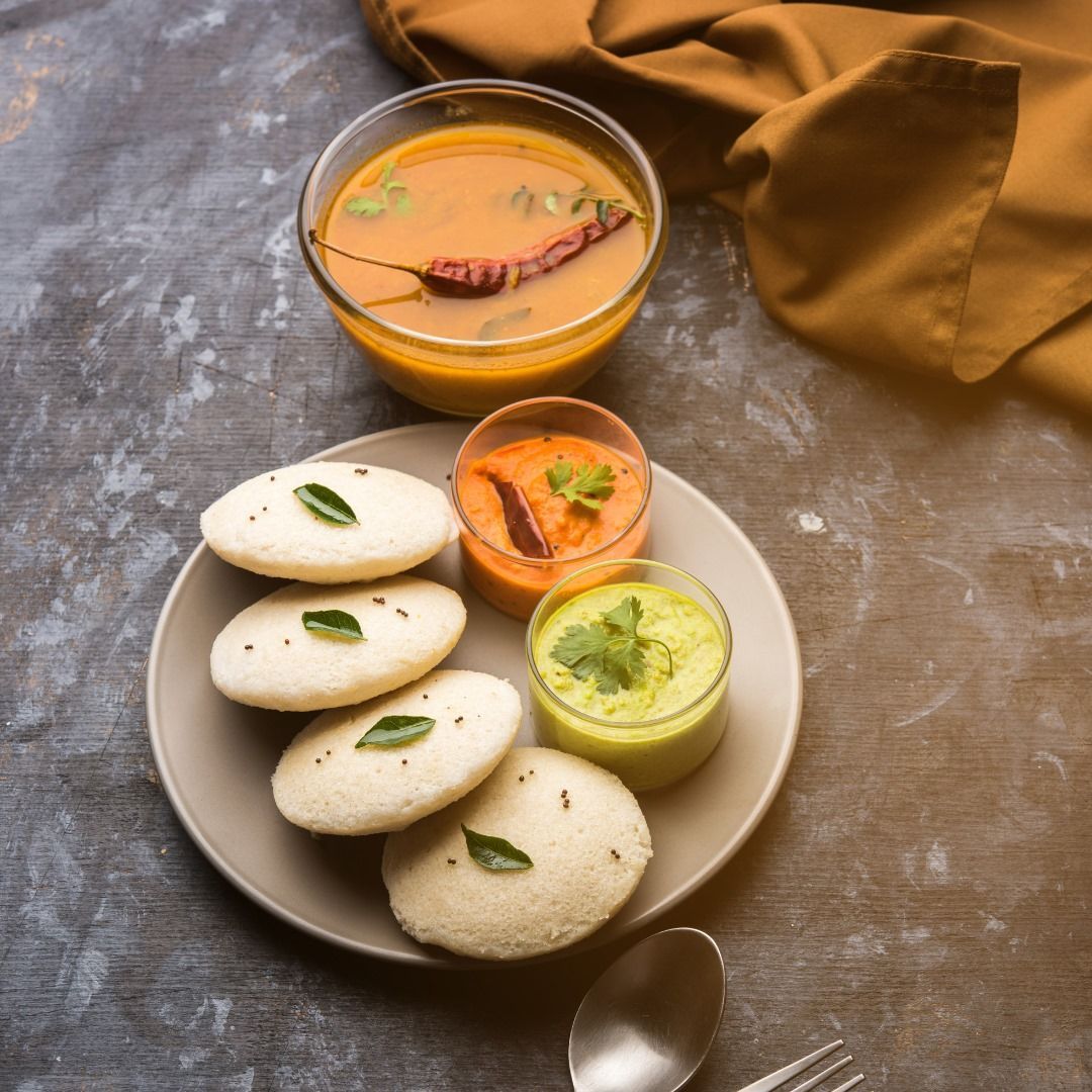 Plate of idli, with sambar and two chutneys. Gray plate on a gray background, with a tan cloth.
