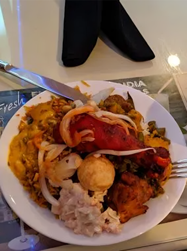 Plate of Indian buffet food: chicken, rice, sauces, and onions. Silverware and black napkins are visible.