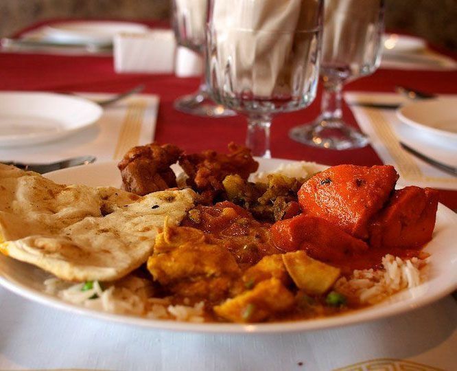 Plate of Indian food: naan, rice, curry, and tandoori chicken, served at a restaurant with glassware and red tablecloth.