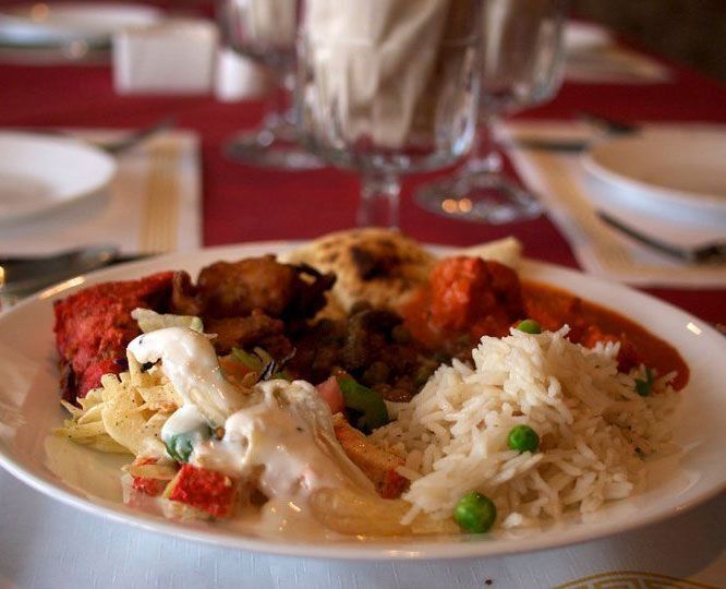Plate of Indian food: rice, chicken, naan, and sauce on a table with glasses.