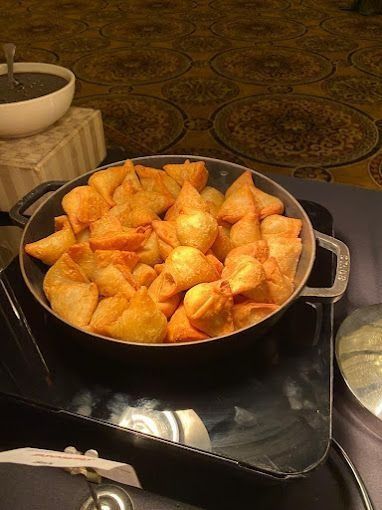 Bowl of golden fried samosas on a buffet with a small bowl of dipping sauce.