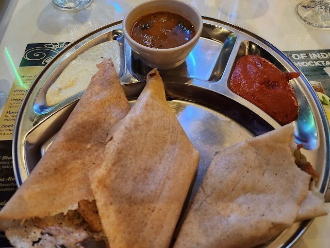 Three folded dosas with dipping sauces on a divided metal plate.