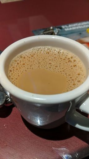 Cup of coffee with foamy top, on a red table.