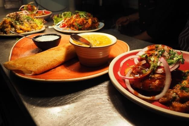 Plates of Indian food: dosa, curry, rice dishes, and appetizers, arranged on a stainless steel surface.