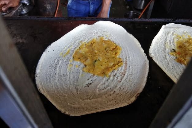Dosa with potato filling on a hot griddle, being prepared at a street food stall.