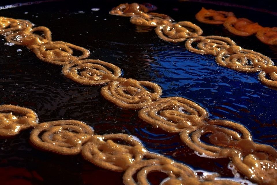 Jalebi pastries frying in hot oil, a close-up. Golden spirals in rows on a black surface.