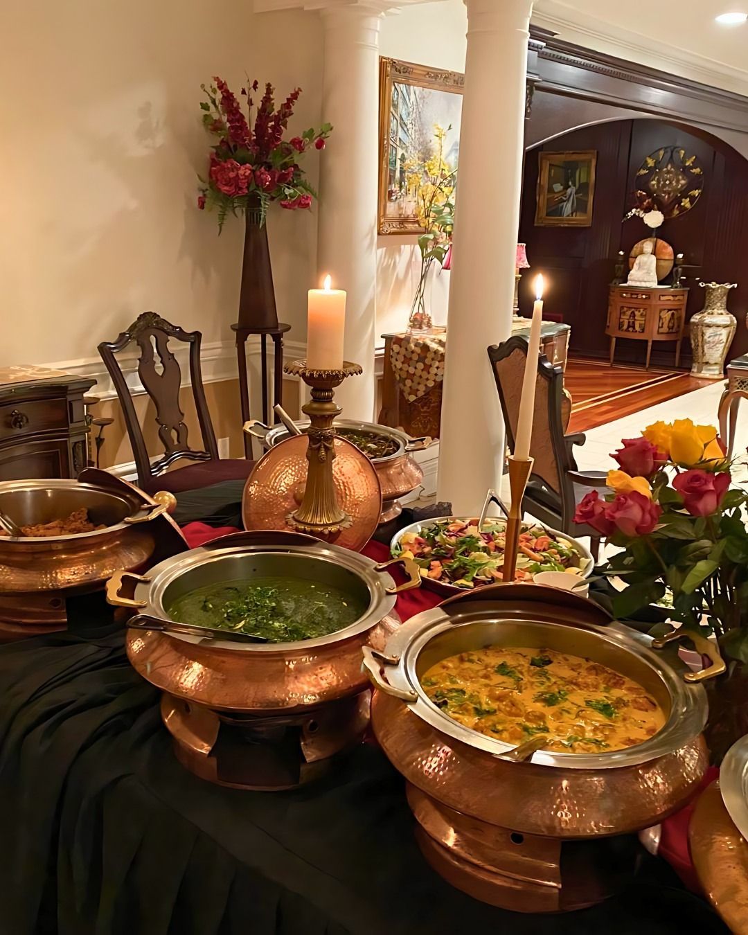 Buffet table with copper dishes, lit candles, and floral decorations.