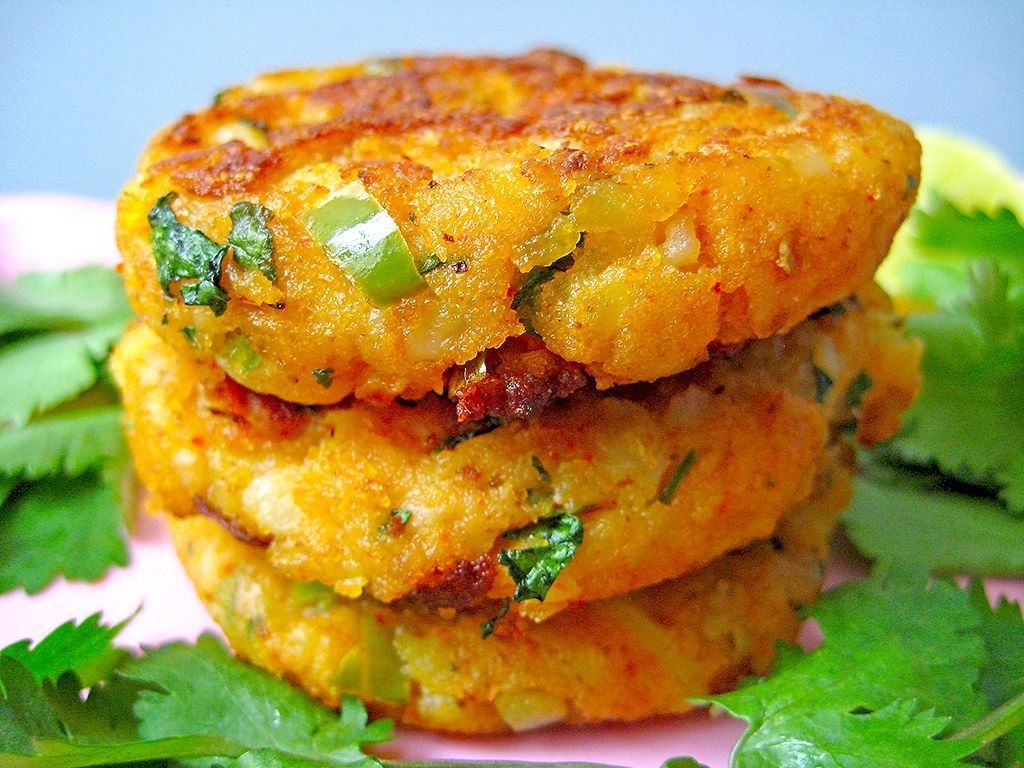 Stack of three golden-brown, round potato cakes with green peppers and cilantro, resting on green herbs.