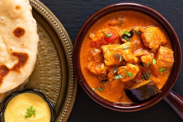 Bowl of chicken curry with naan bread and sauce on a tray.