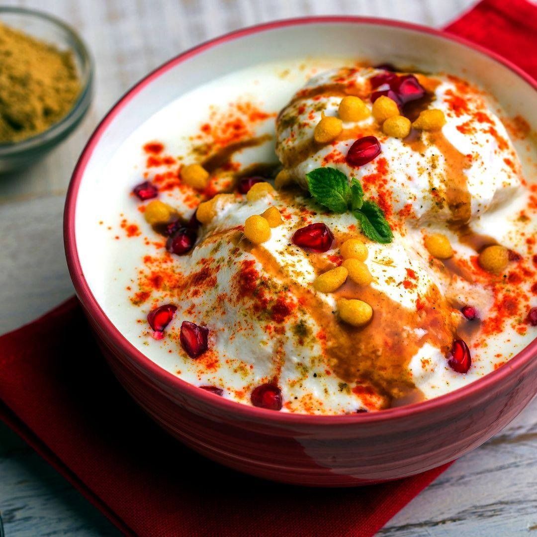 Bowl of dahi vada topped with garnishes like pomegranate seeds, spiced chickpeas, and spices.