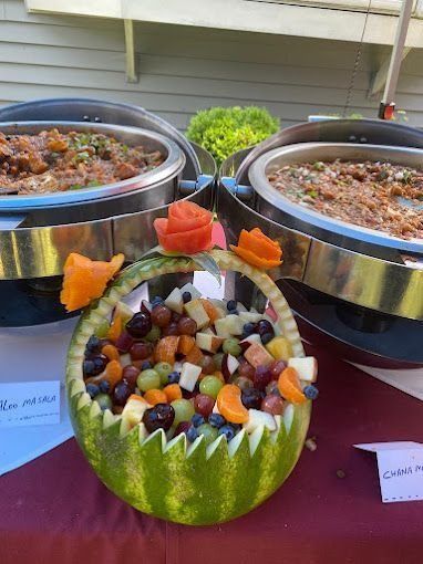 Watermelon fruit basket with colorful fruit, flanked by two chafing dishes.