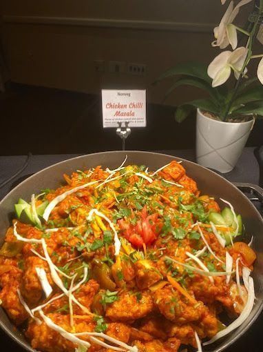 Chicken chili masala in a large bowl, garnished with cucumber, cabbage, and cilantro.