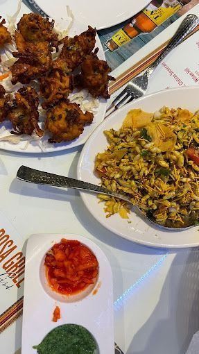 Plated Indian dishes: vegetable fritters, puffed rice snack, and red and green sauces.