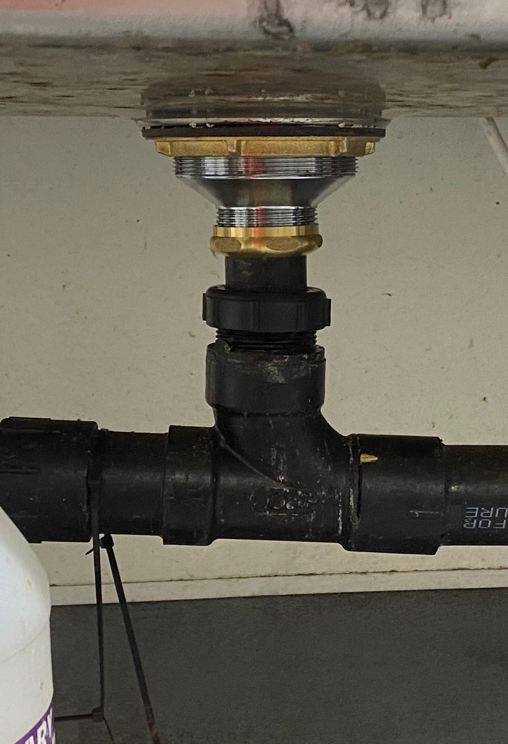 Black plumbing fixture under a surface, with a clear top and a gold-colored ring.